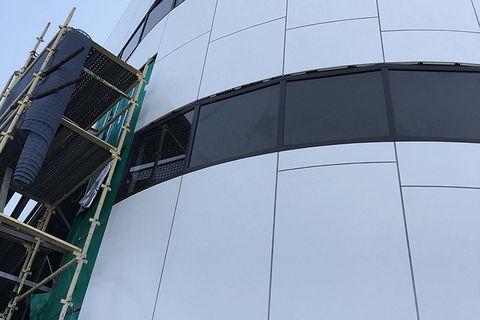 A curved panel facade with scaffolding at one end, during installation.